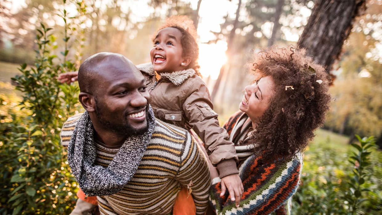 A family of three smiles outdoors