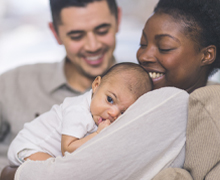 A father looks on as a mother holds a baby