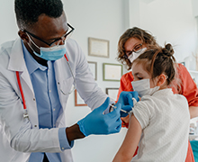 Doctor giving a young girl a flu shot in her arm while her mom watches.