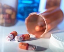 An open bottle of pills laying on its side with three pills spilled onto the counter