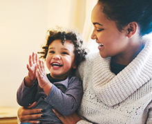 A mother happily looking down at her infant who is smiling and clapping