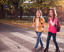 Two girls wearing backpacks are walking in a crosswalk across the street