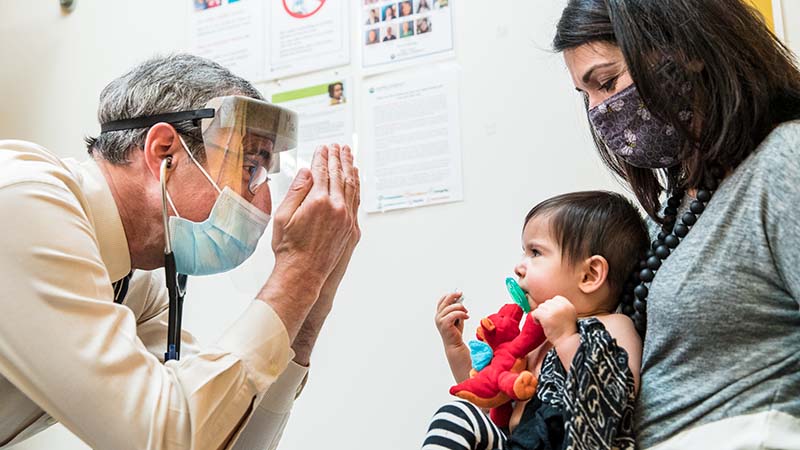 A doctor plays peek-a-boo with a baby held by their mother