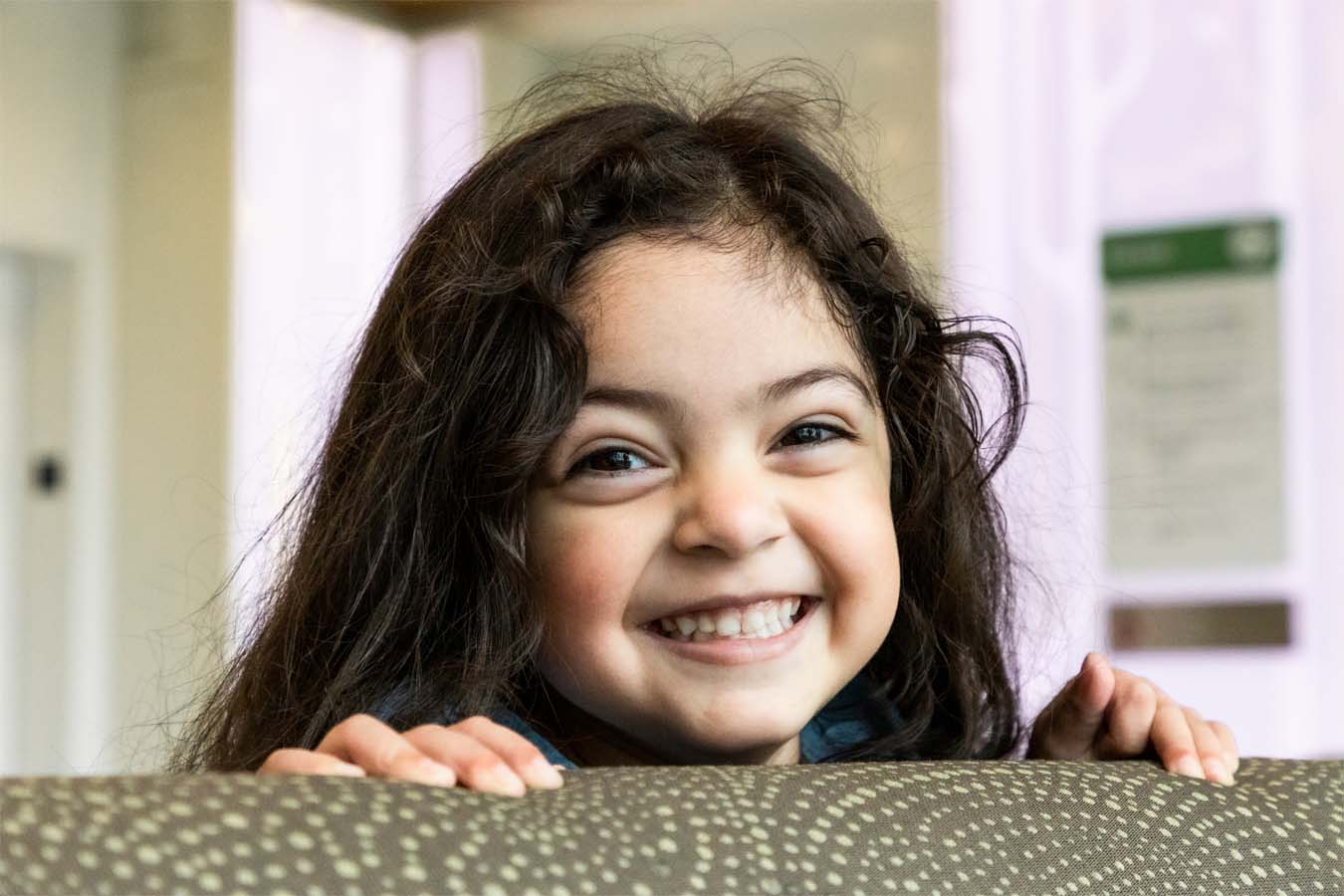 Aliyanna peeks over the top of a couch